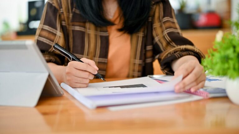 Étudiant rédigeant son rapport d’alternance devant un ordinateur, avec des notes et des documents professionnels sur le bureau.